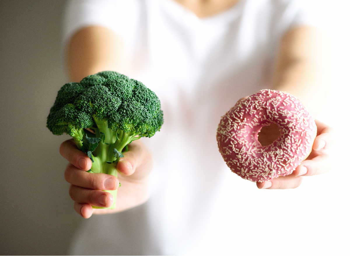 close-up woman holding up broccoli and donut