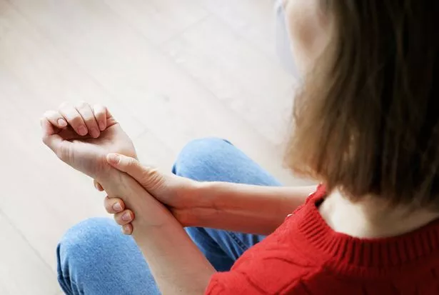 Beautiful blonde woman suffering from wrist bone pain while sitting on sofa at home.