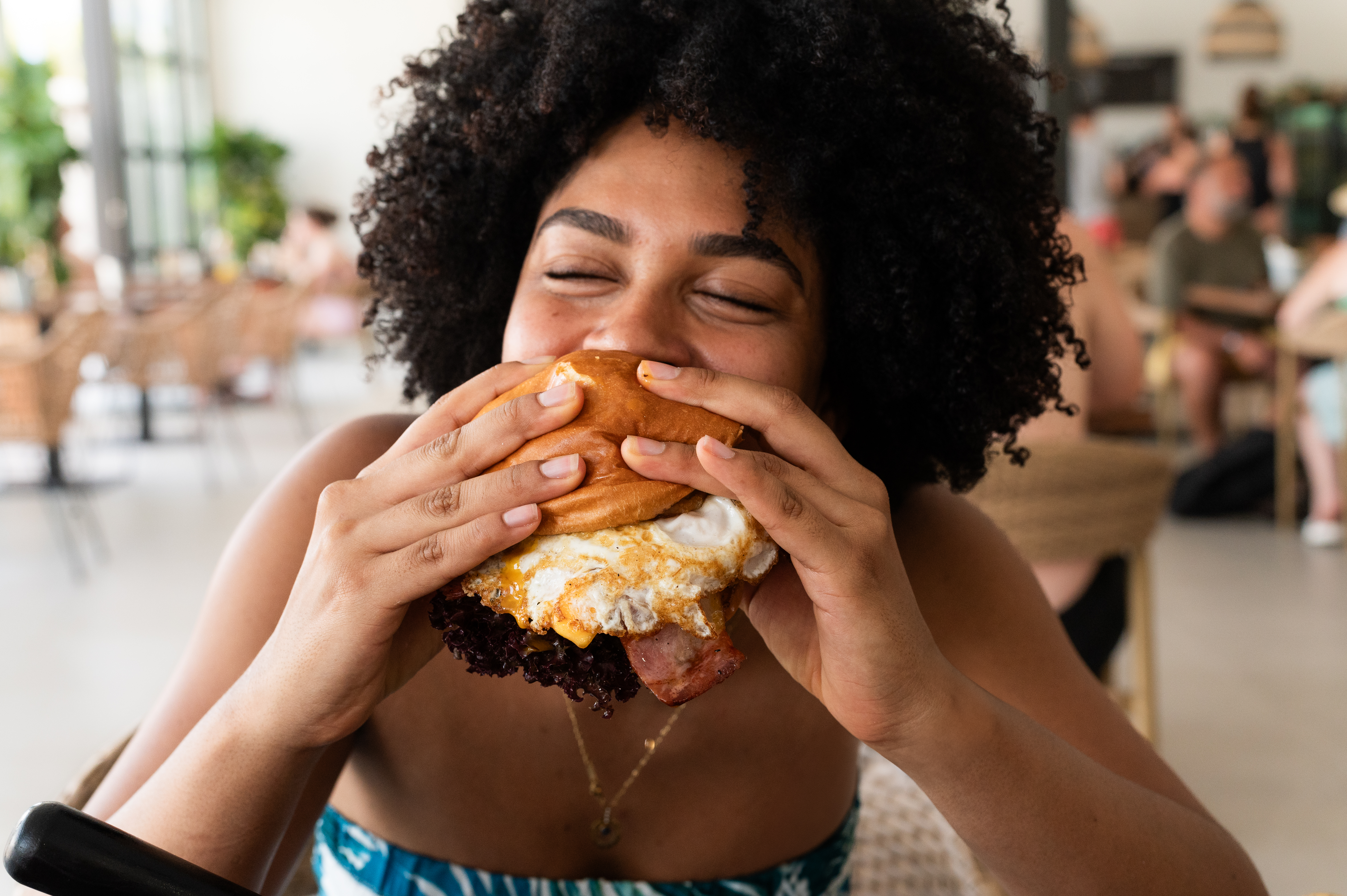 Young woman with closed eyes eating a cheeseburger with egg and bacon.