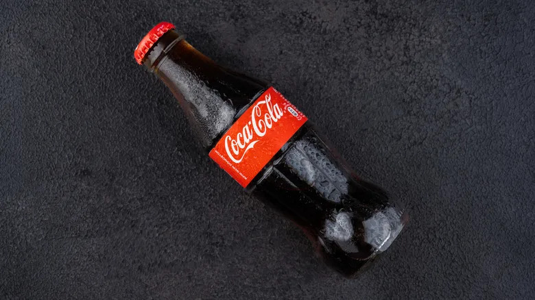 Glass bottle of Coca-Cola on dark surface